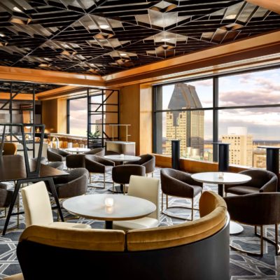 Lounge de primer nivel con mesas, sillas y vista a la ciudad a través de ventanas del piso al techo